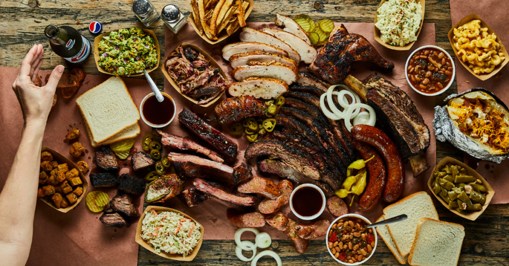 Different styles of Texan BBQ meats are placed on the table with breads, sides, and sauces